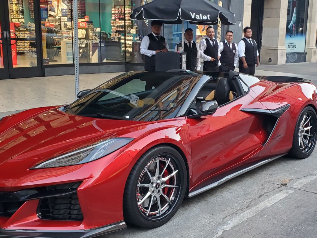 Uniformed valet team posing with red Corvette at premium parking service in Los Angeles
