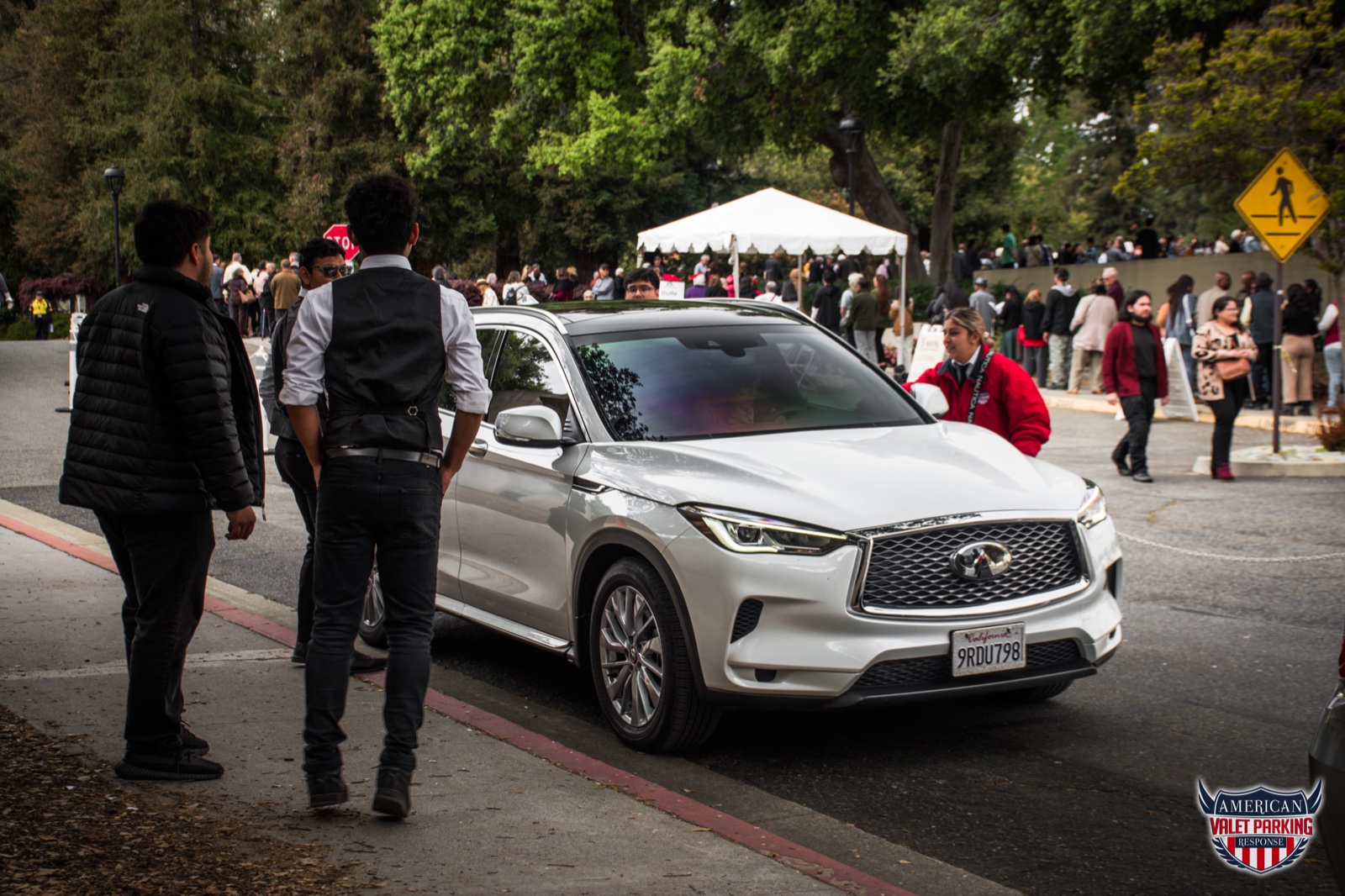 Uniformed valet attendants welcoming guests beside a white SUV at an outdoor event