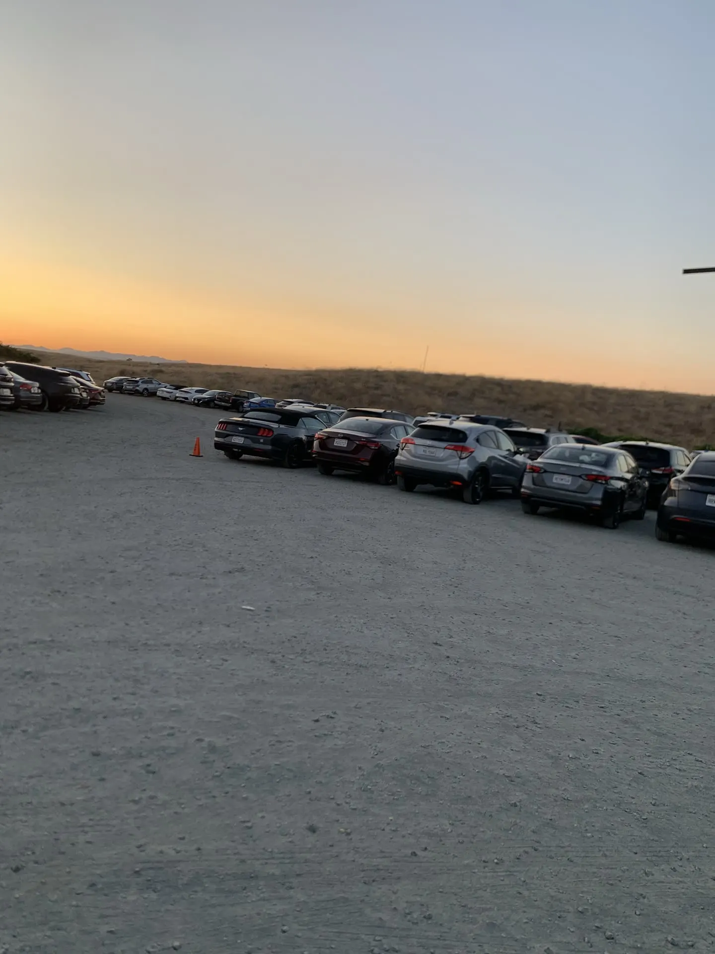Rows of parked cars beside a wide driving aisle at sunset