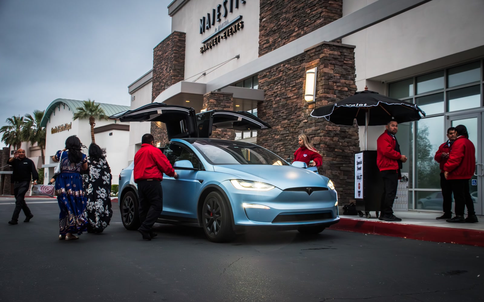 Valet attendants assisting guests beside a blue vehicle at a venue entrance